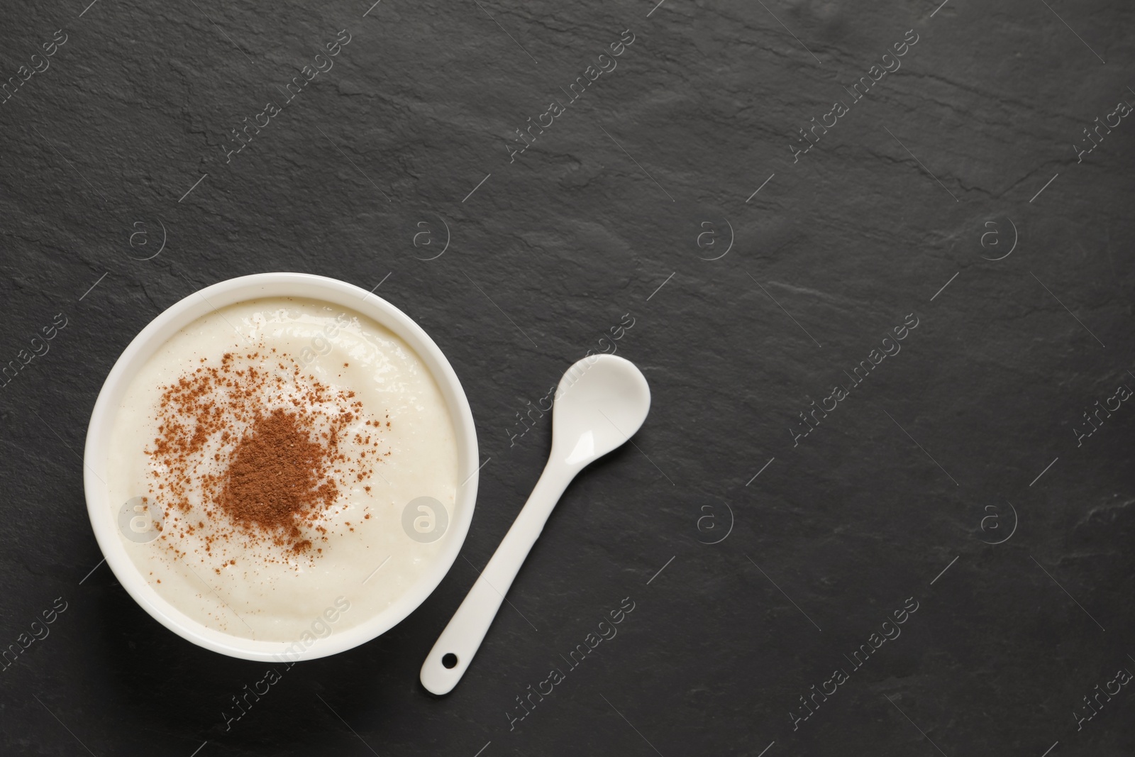 Photo of Delicious semolina pudding with cinnamon and spoon on black table, flat lay. Space for text