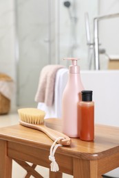 Photo of Bottles of shower gels and brush on wooden table near tub in bathroom