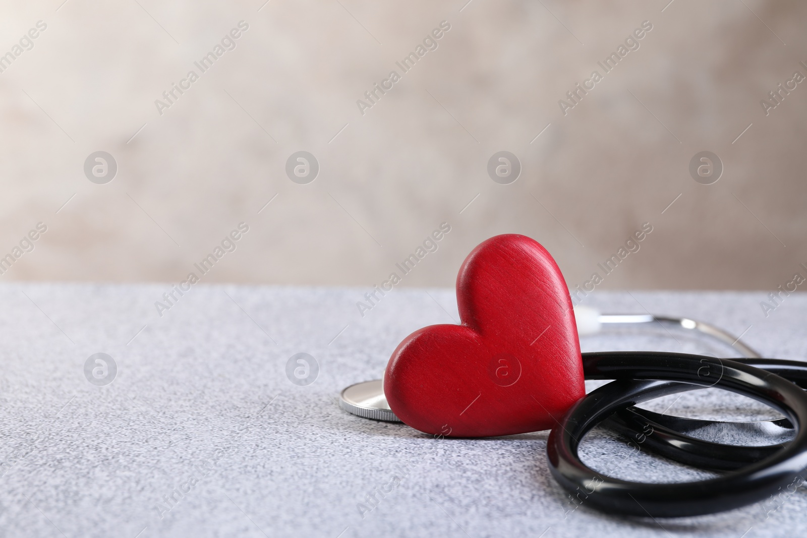 Photo of Stethoscope and red heart on grey stone table. Space for text