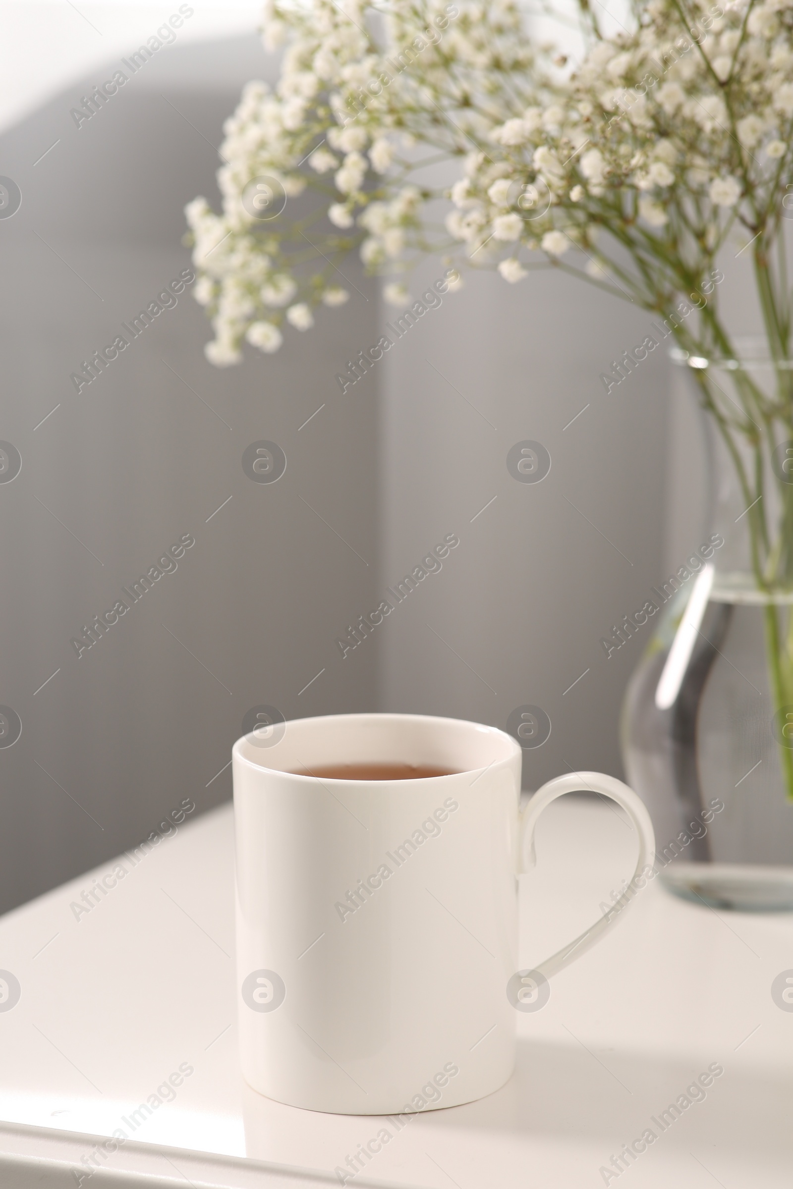 Photo of Ceramic mug with tea on white bedside table indoors. Mockup for design