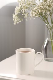 Photo of Ceramic mug with tea on white bedside table indoors. Mockup for design