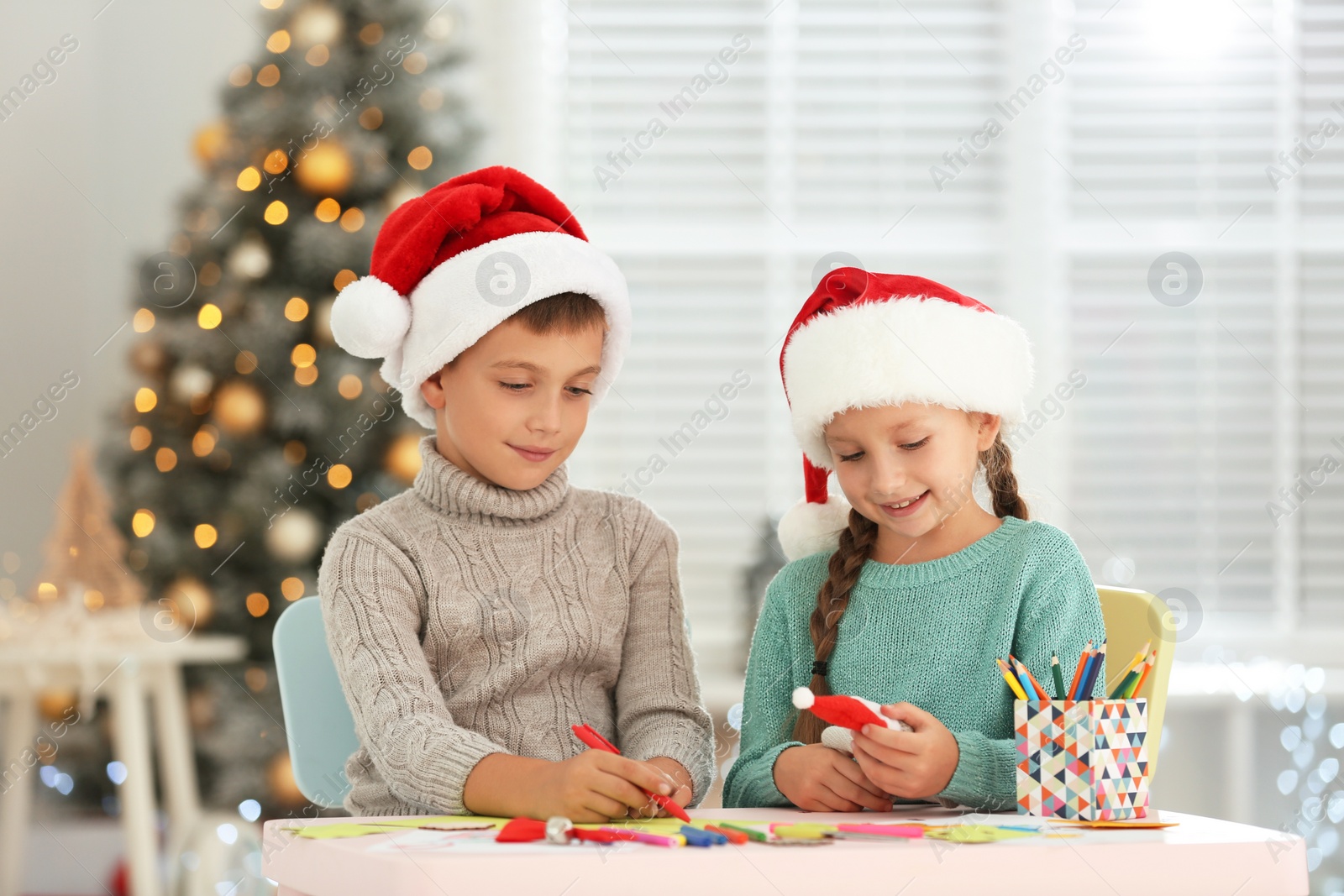 Photo of Little children in Santa hats making craftworks at table indoors. Christmas season