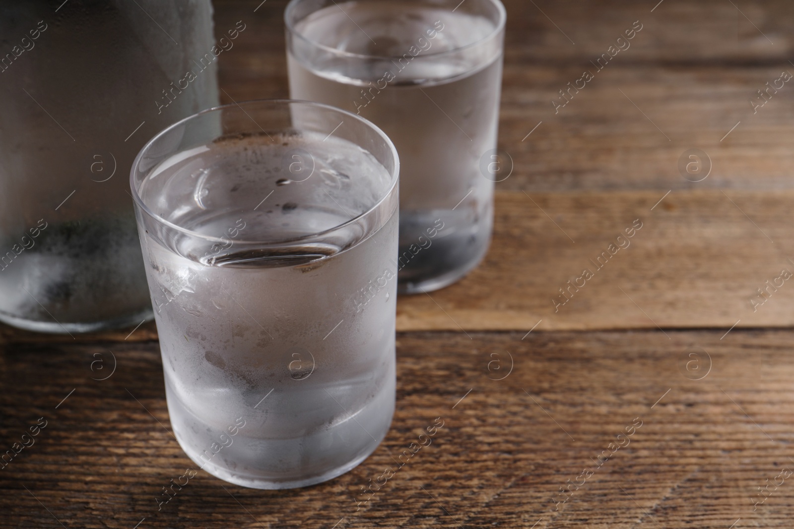 Photo of Vodka in shot glasses on wooden table, closeup. Space for text