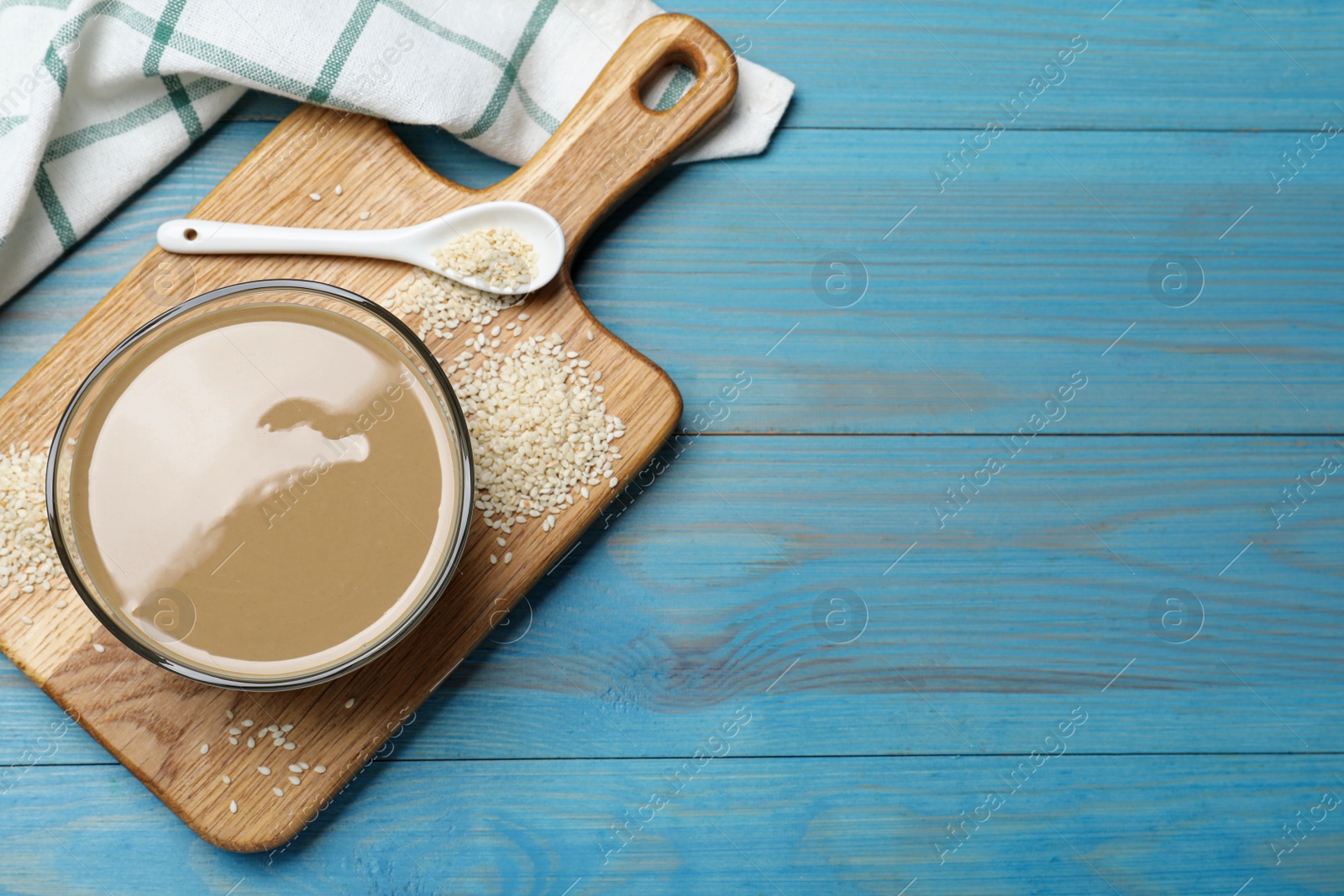 Photo of Tasty sesame paste, seeds and spoon on light blue wooden table,top view. Space for text