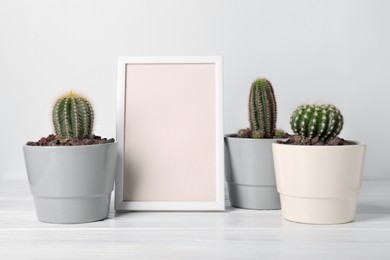 Photo of Different cacti in pots and frame on white wooden table