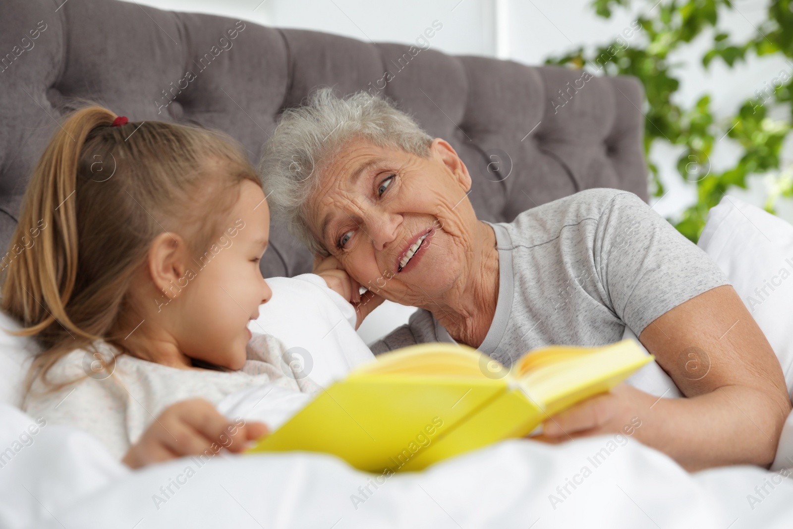 Photo of Cute girl and her grandmother reading book on bed at home