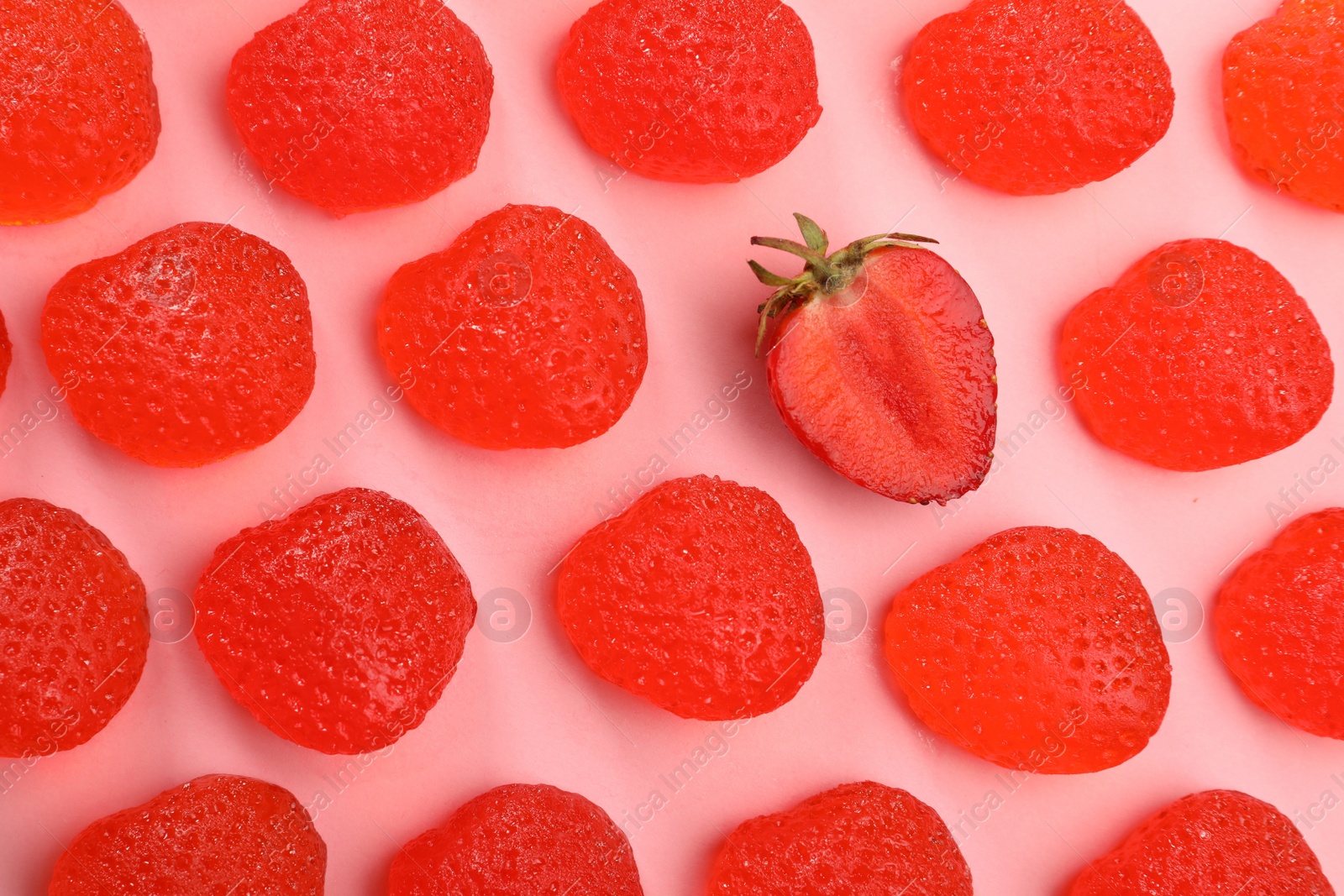 Photo of Delicious gummy candies and fresh strawberry on pink background, flat lay