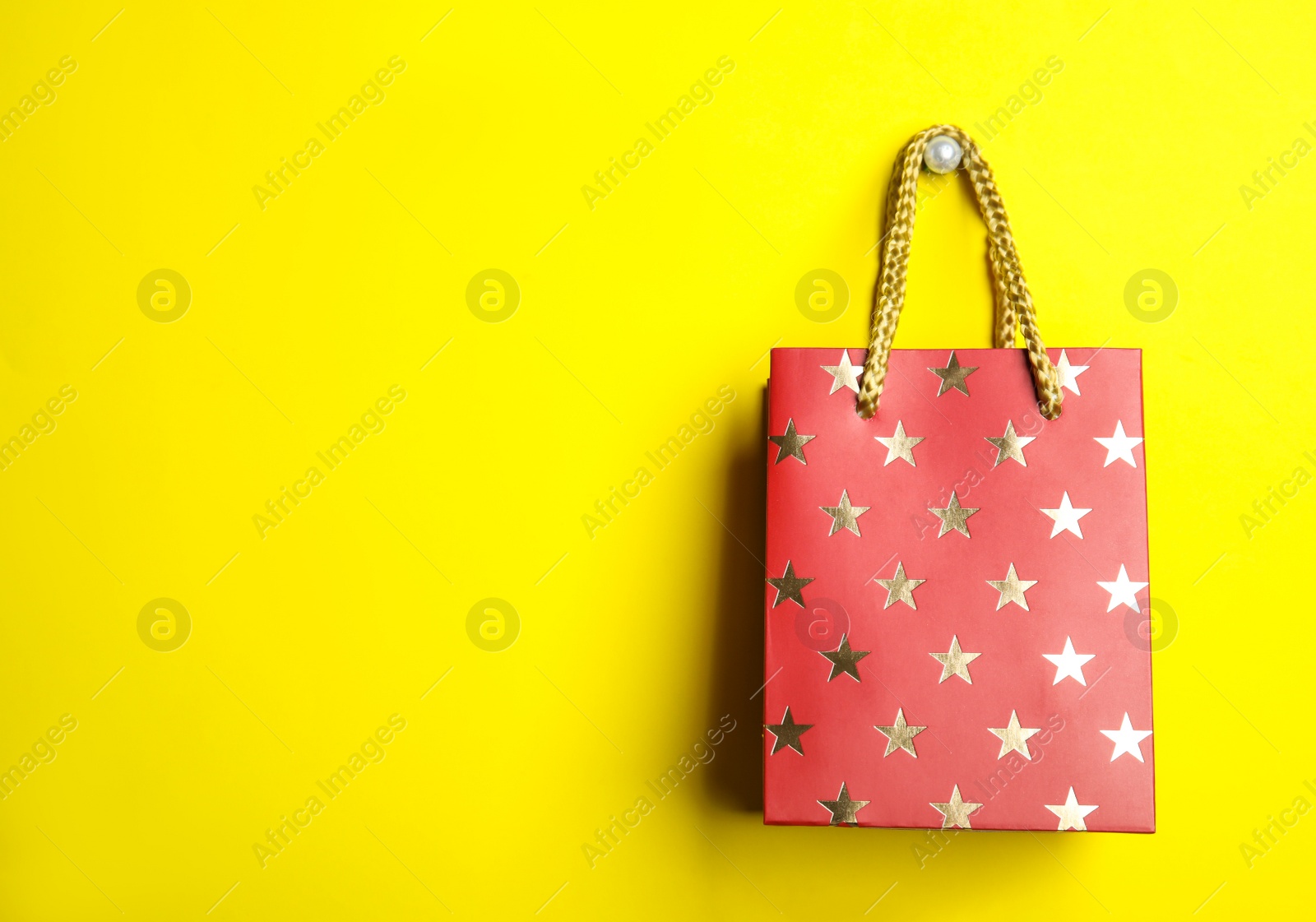 Photo of Red shopping paper bag with star pattern on yellow background, space for text