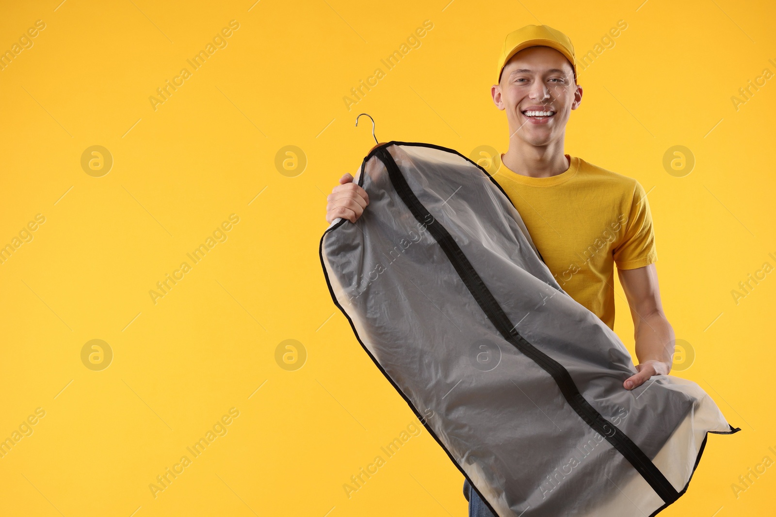 Photo of Dry-cleaning delivery. Happy courier holding garment cover with clothes on orange background, space for text