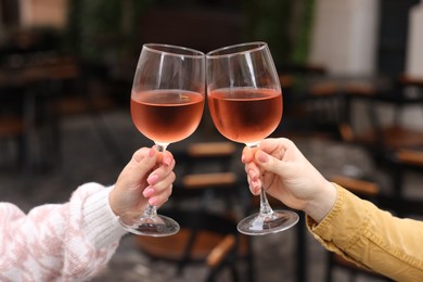 Women clinking glasses with rose wine in outdoor cafe, closeup