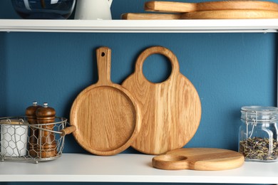 Photo of Wooden cutting boards, kitchen utensils and dry tea on shelving unit near blue wall