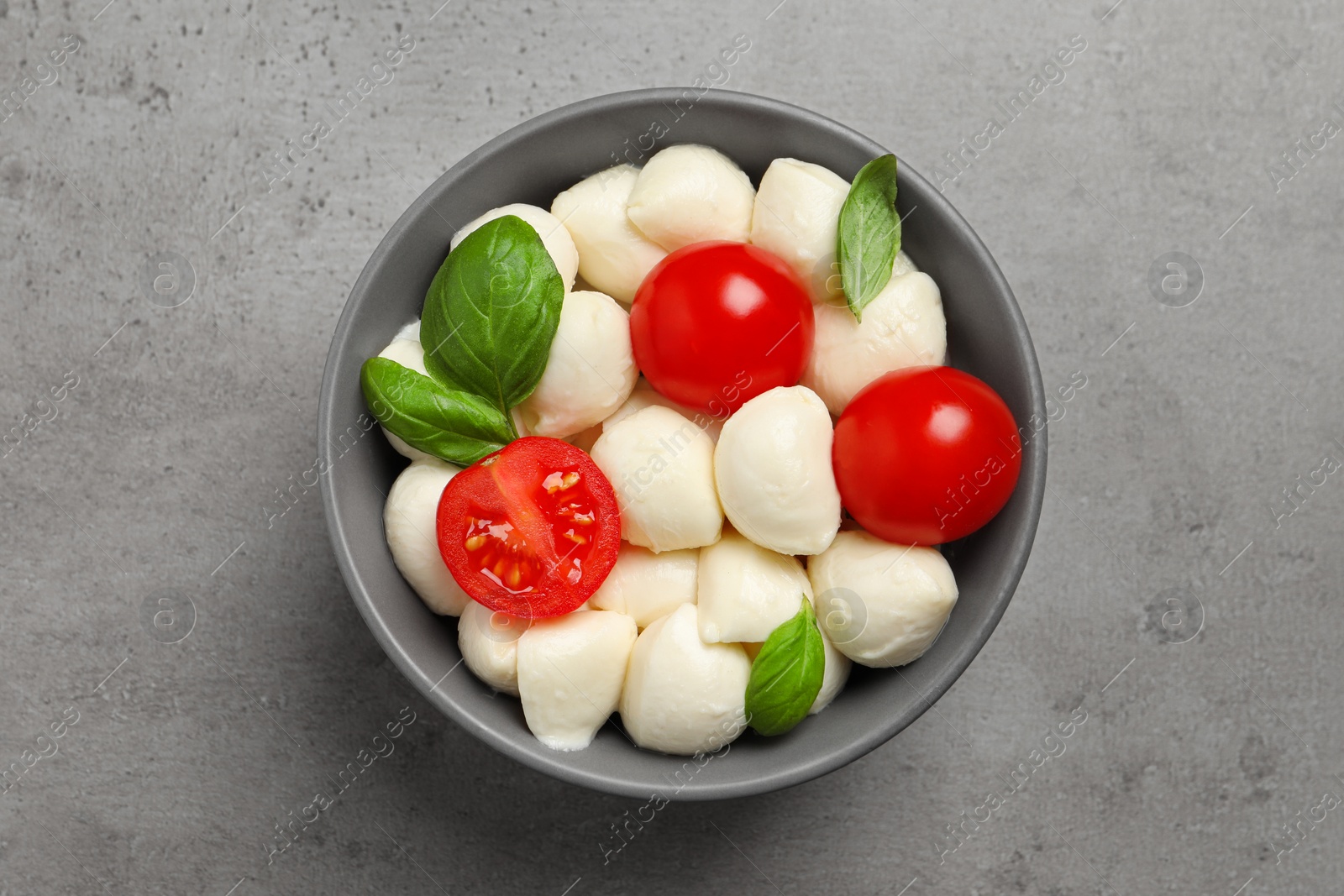 Photo of Delicious mozzarella balls, tomatoes and basil leaves on light gray table, top view