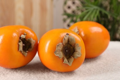 Photo of Delicious ripe persimmons on light textured table indoors, closeup