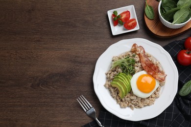 Photo of Tasty boiled oatmeal with fried egg, avocado and bacon served on wooden table, flat lay. Space for text