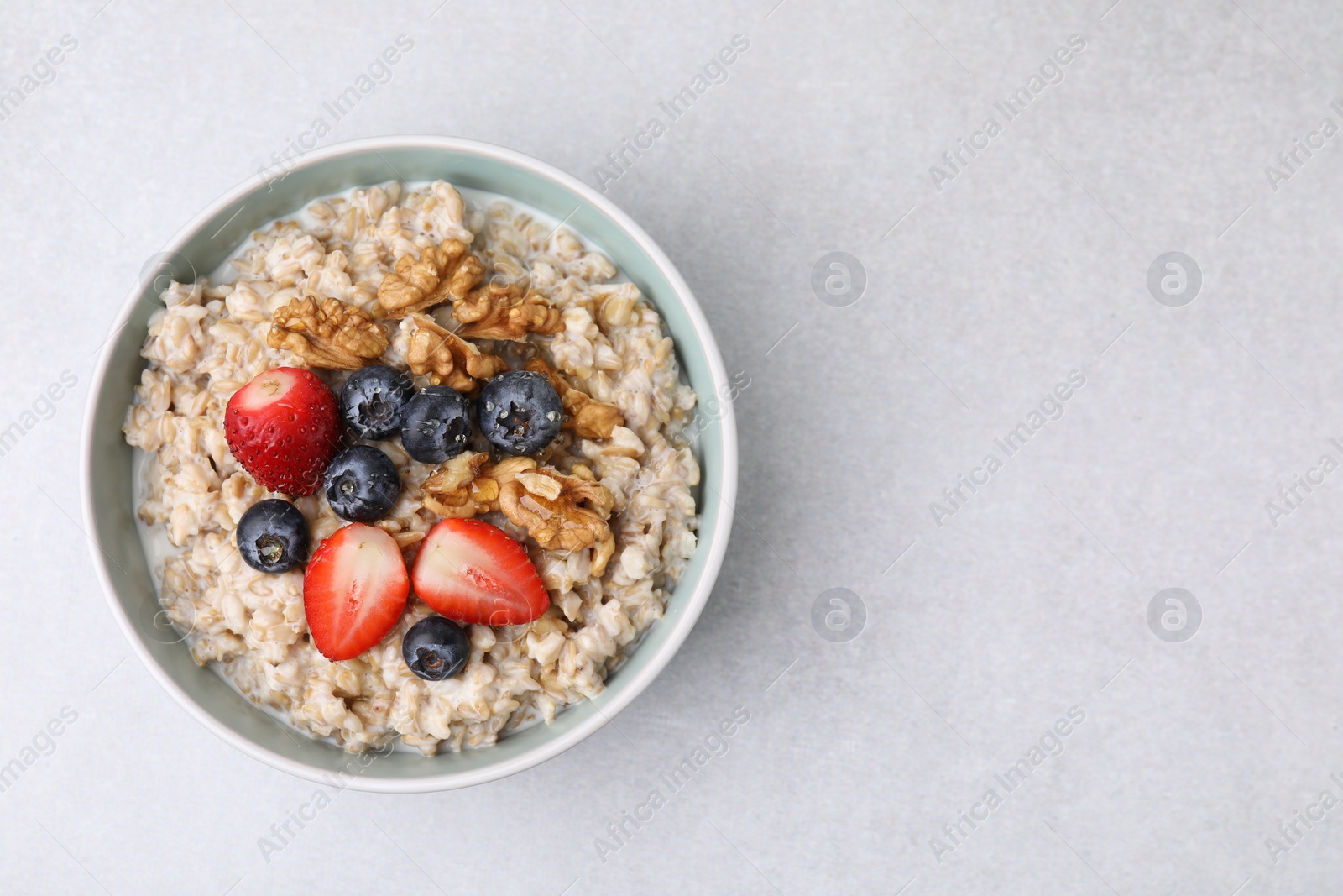 Photo of Tasty oatmeal with strawberries, blueberries and walnuts in bowl on grey table, top view. Space for text