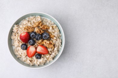 Photo of Tasty oatmeal with strawberries, blueberries and walnuts in bowl on grey table, top view. Space for text