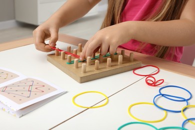 Motor skills development. Girl playing with geoboard and rubber bands at white table indoors, closeup