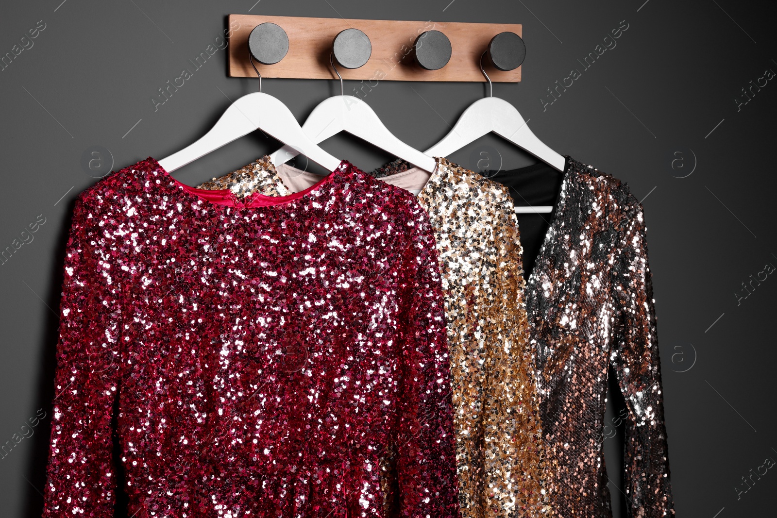 Photo of Different shiny beautiful women's party dresses on hangers near grey wall. Stylish trendy clothes for high school prom