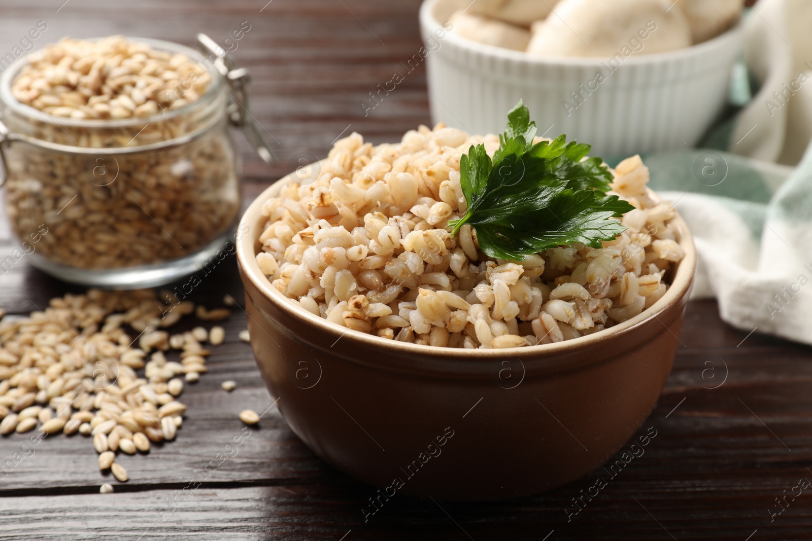 Photo of Delicious pearl barley with parsley in bowl on wooden table