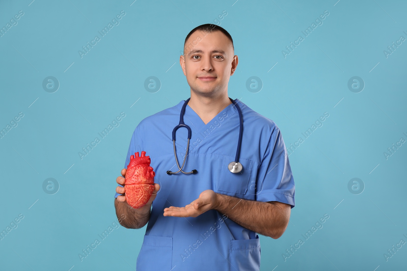 Photo of Doctor with stethoscope and model of heart on light blue background. Cardiology concept