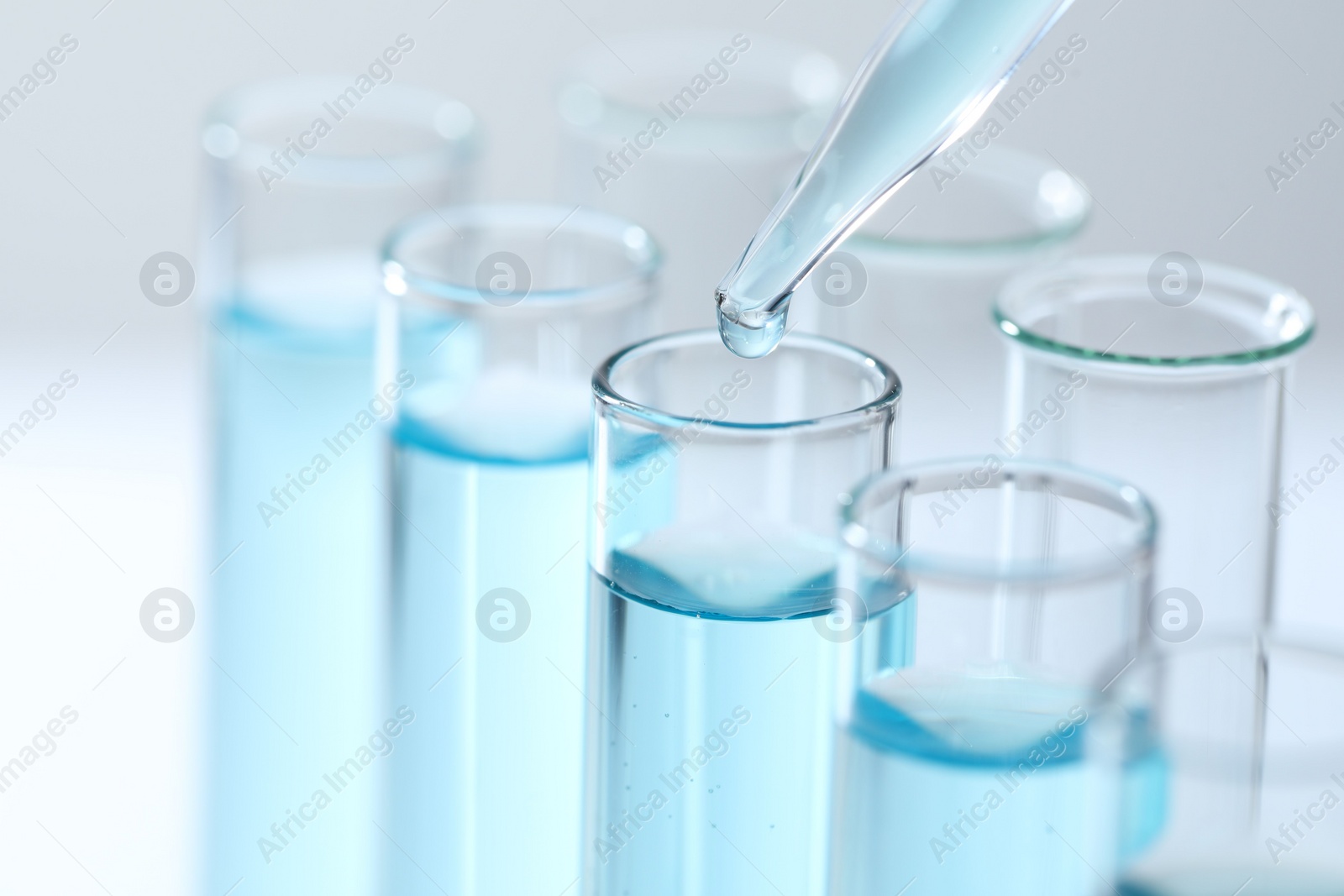 Photo of Dripping liquid from pipette into test tube on light background, closeup