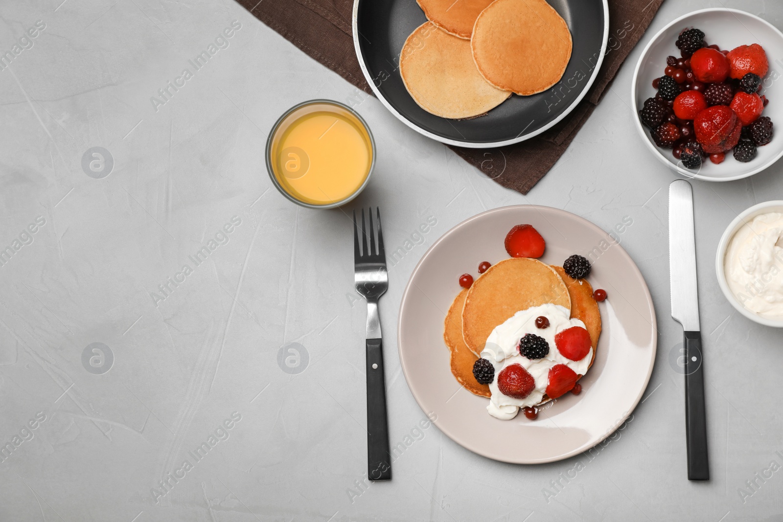 Photo of Delicious pancakes with berries, sour cream and glass of juice served for breakfast on table