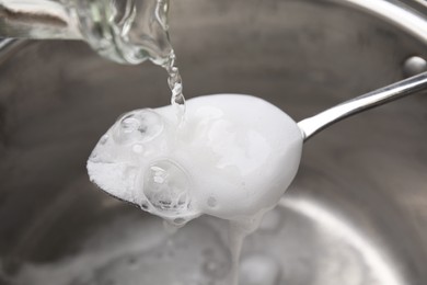 Photo of Pouring vinegar into spoon with baking soda over saucepan, closeup