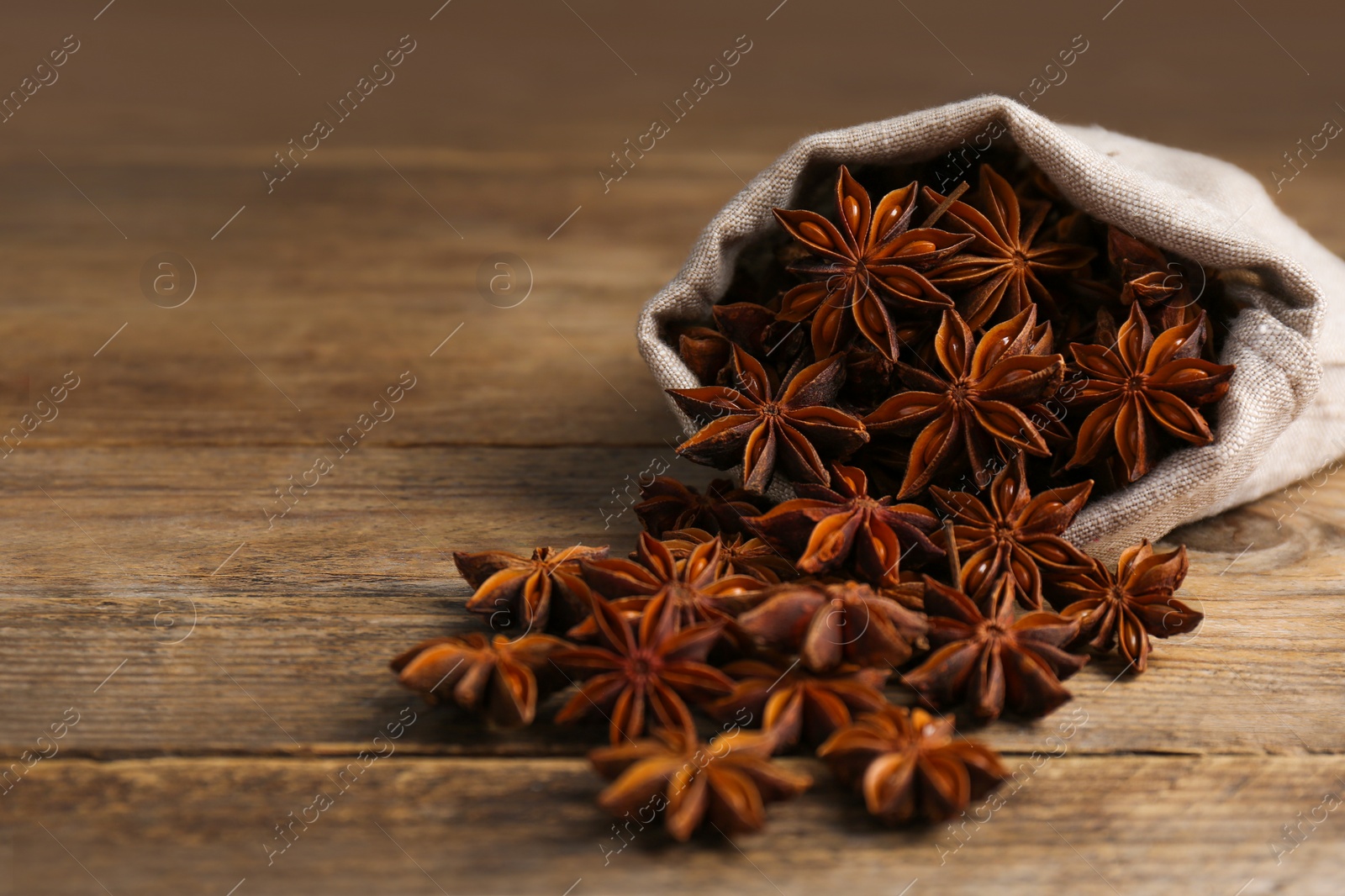 Photo of Overturned bag with aromatic anise stars on wooden table, closeup. Space for text