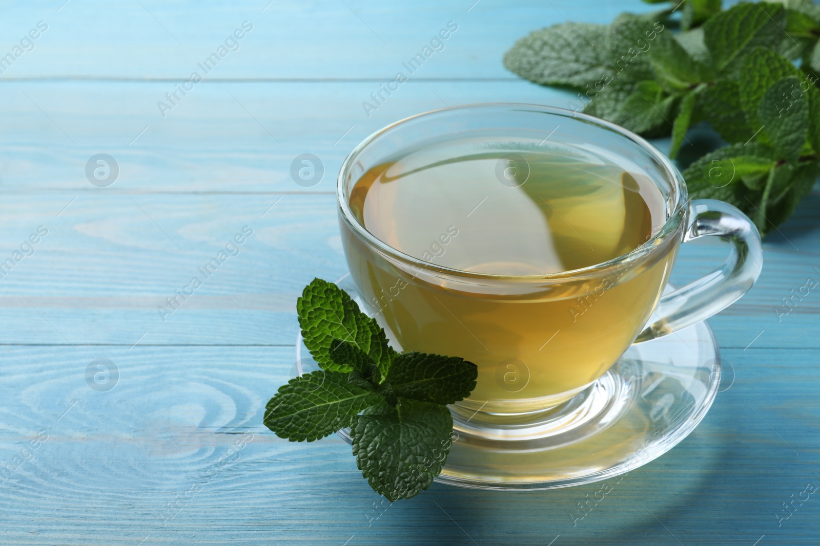 Photo of Cup of hot aromatic mint tea on light blue wooden table. Space for text