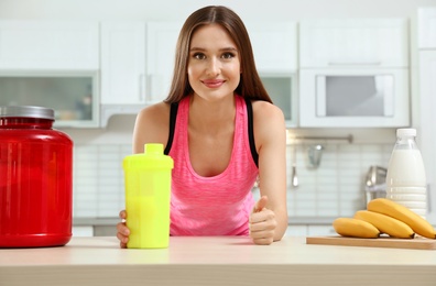 Young woman with bottle of protein shake in kitchen