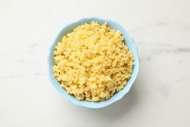 Tasty millet porridge in bowl on white marble table, top view