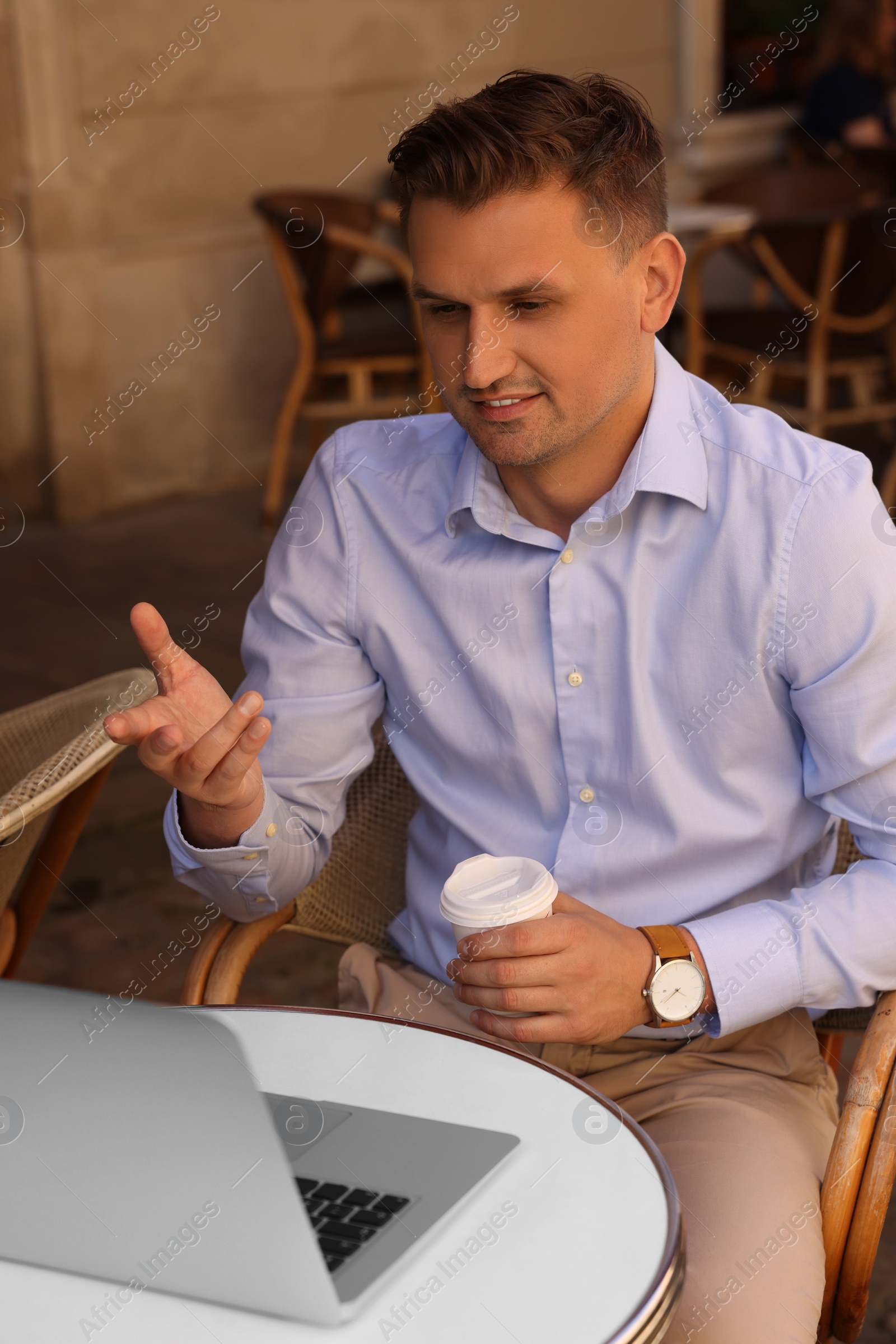 Photo of Handsome man with cup of coffee working on laptop at table in outdoor cafe