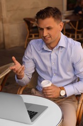 Handsome man with cup of coffee working on laptop at table in outdoor cafe