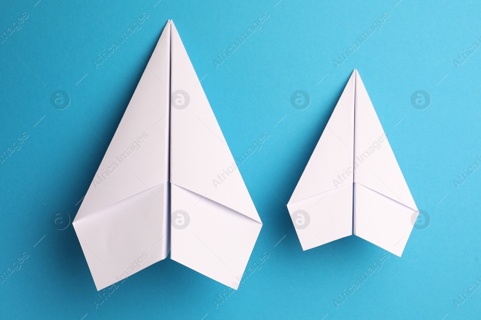 Photo of Handmade white paper planes on light blue background, flat lay