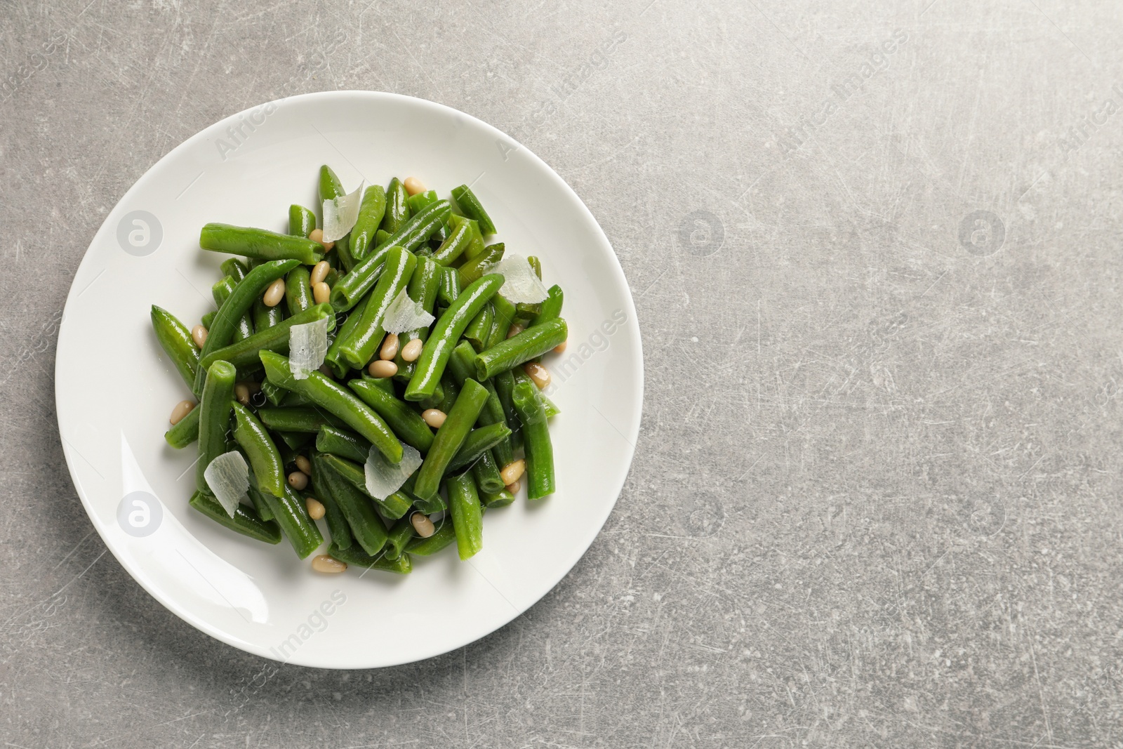 Photo of Plate of tasty salad with green beans on light grey table, top view. Space for text