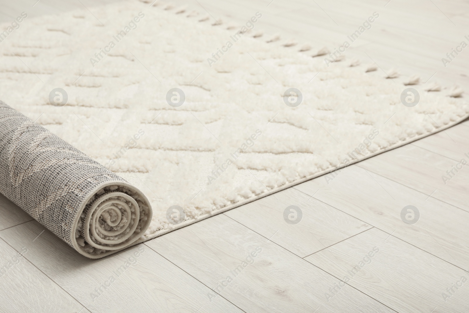 Photo of Rolled white carpet with beautiful pattern on floor, closeup. Space for text