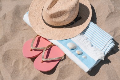 Photo of Straw hat, beach towel, seashells and flip flops on sand