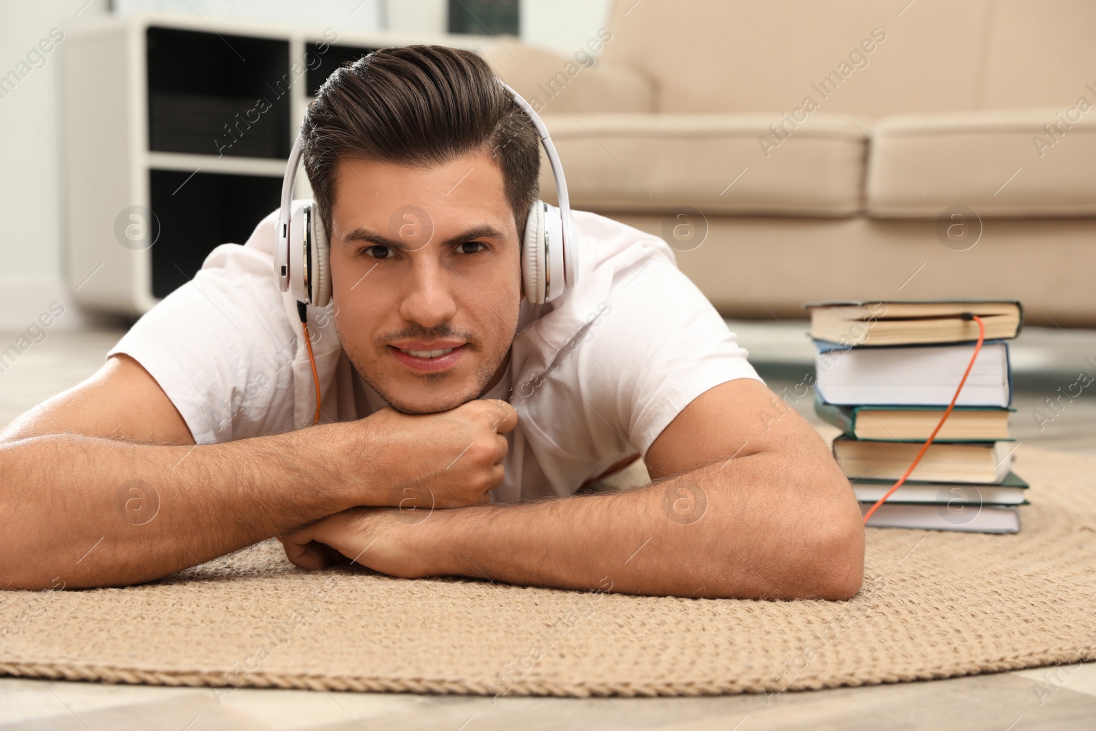 Photo of Man with headphones connected to book
on floor at home. Audiobook concept