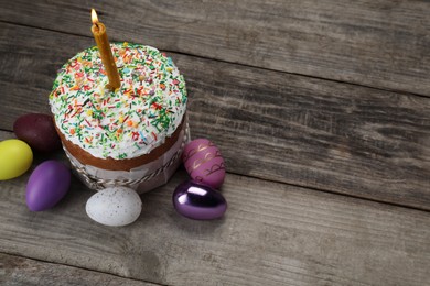 Photo of Traditional Easter cake with sprinkles, burning candle and painted eggs on wooden table, above view. Space for text