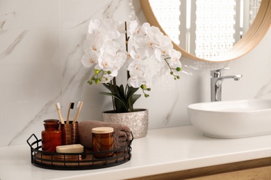Photo of Beautiful flowers and different toiletries near vessel sink in bathroom