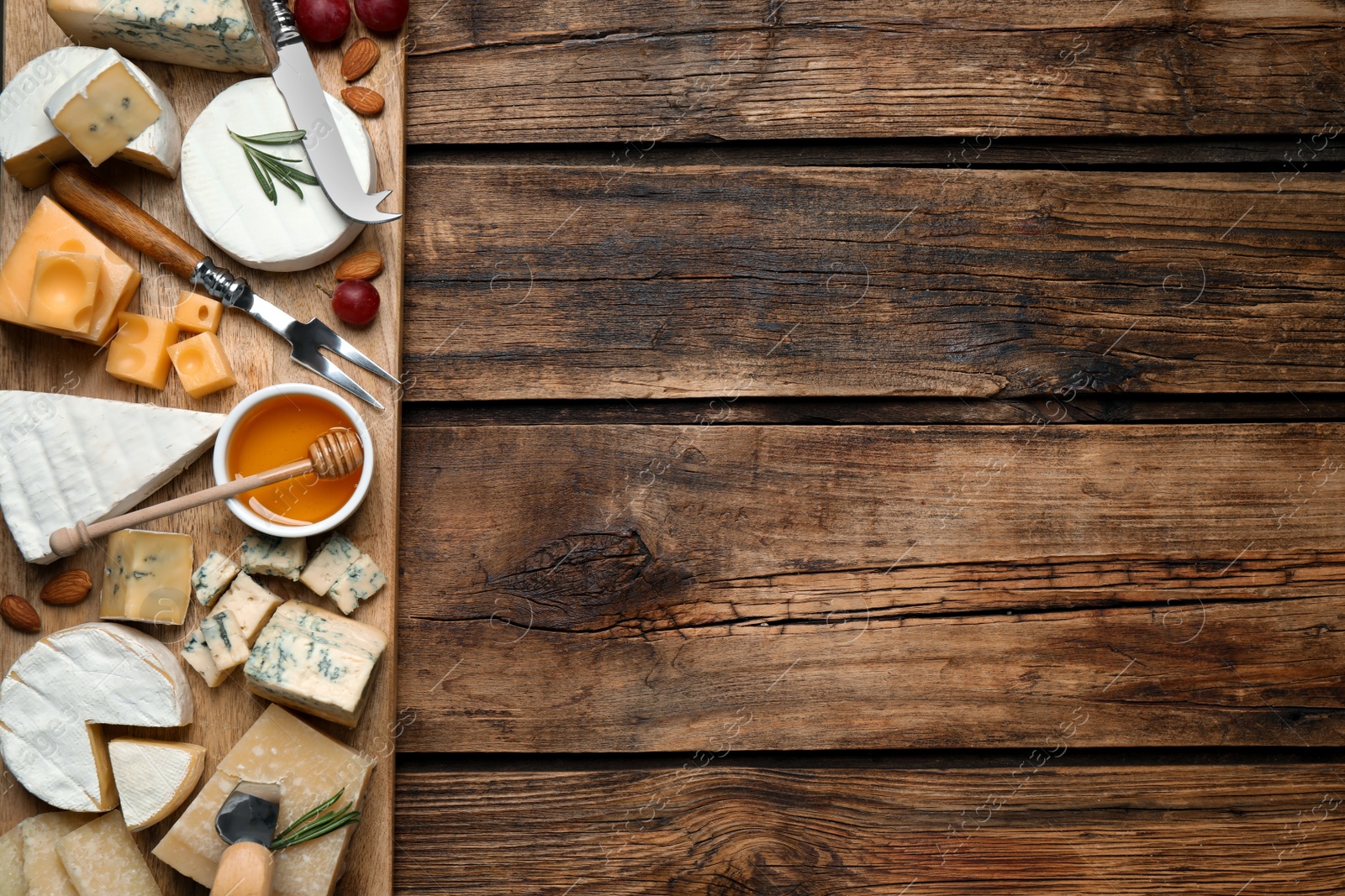 Photo of Cheese platter with specialized knife and fork on wooden table, flat lay. Space for text