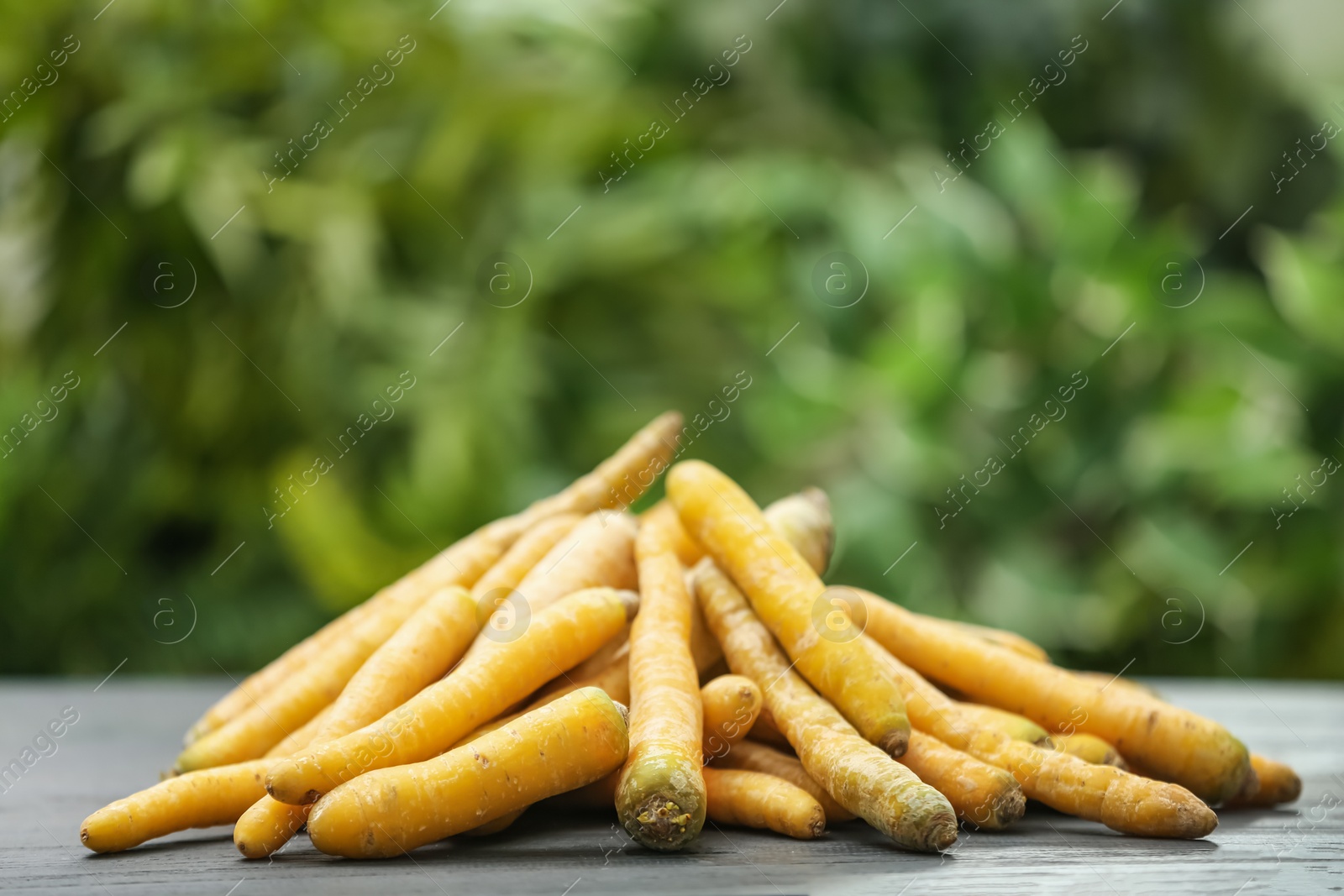 Photo of Raw yellow carrots on wooden table against blurred background