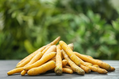 Photo of Raw yellow carrots on wooden table against blurred background