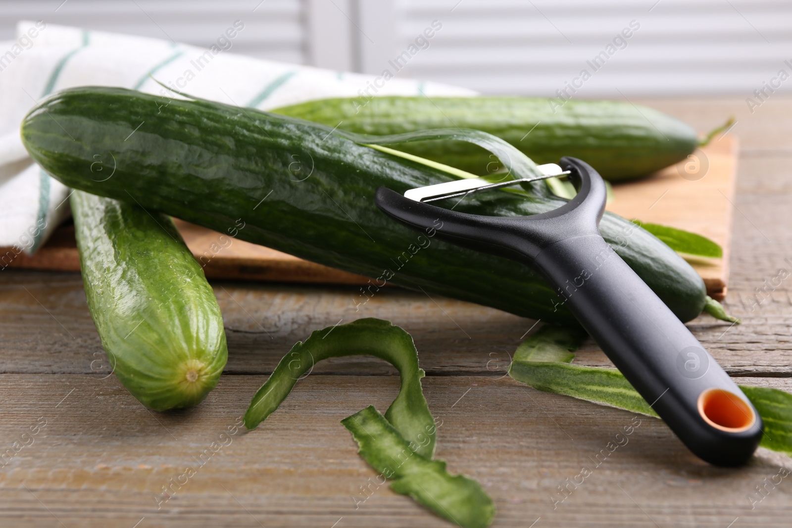 Photo of Fresh cucumbers, peels and peeler on wooden table, closeup