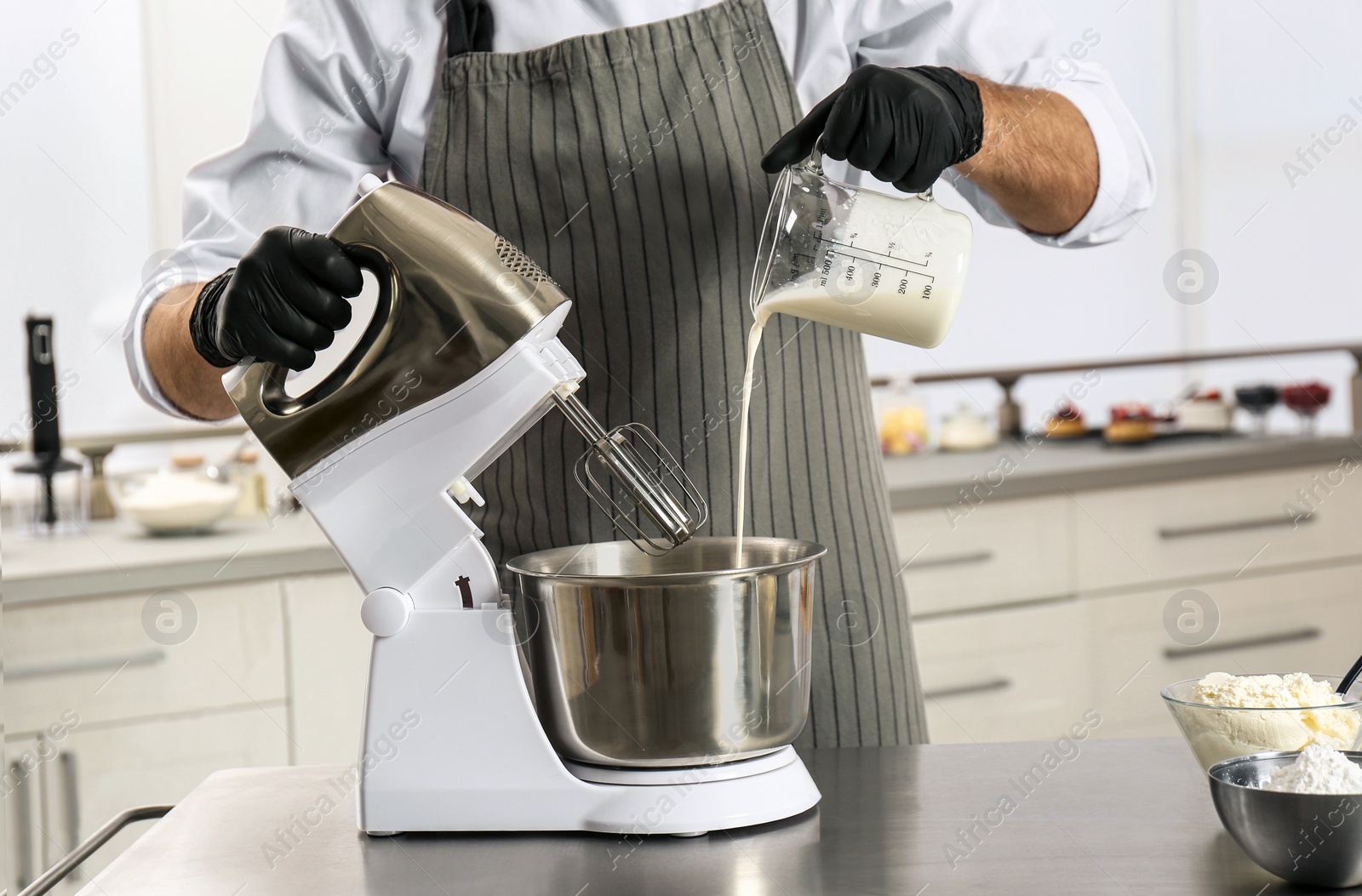 Photo of Male pastry chef preparing dough in mixer at kitchen table, closeup