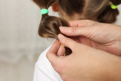 Photo of Professional stylist braiding girl's hair indoors, closeup