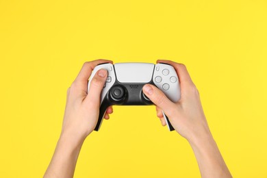 Woman using game controller on yellow background, closeup