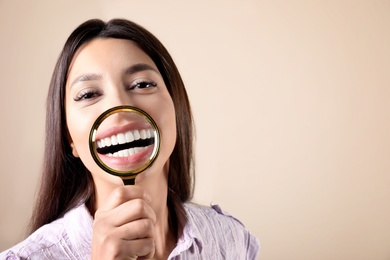 Young woman with healthy teeth and magnifier on color background. Space for text