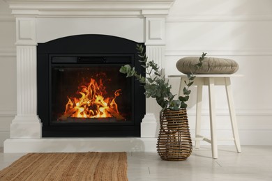 Beautiful eucalyptus branches in vase and stool near fireplace indoors