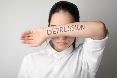 Photo of Young woman hiding face behind hand with written word DEPRESSION on light background